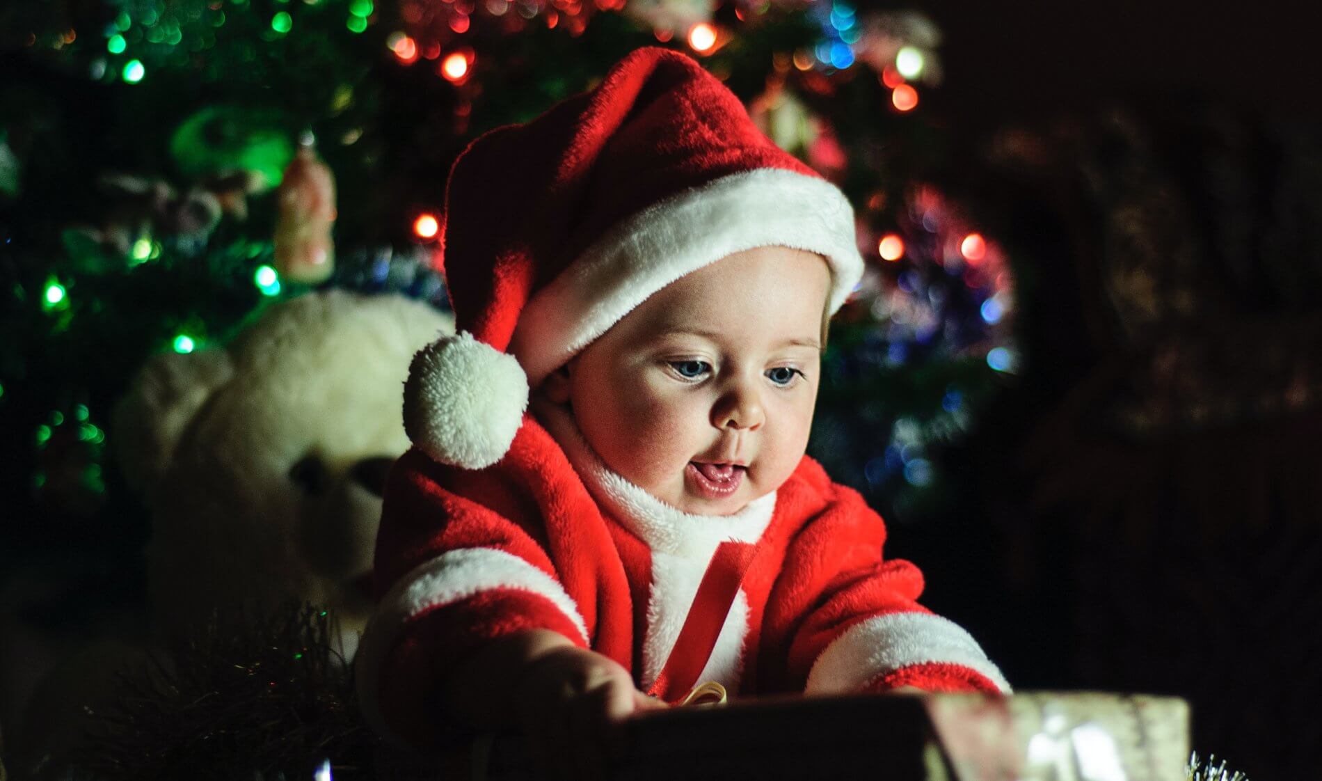 Baby opening present in a little Santa suit