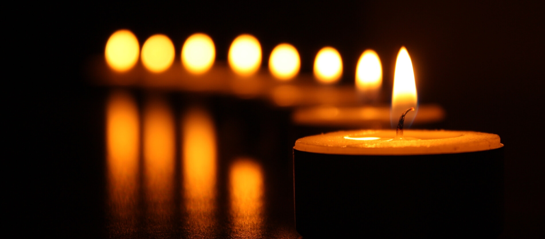 Lit candles with the first candle in focus and other remaining candles blurred in the background in a vertical line