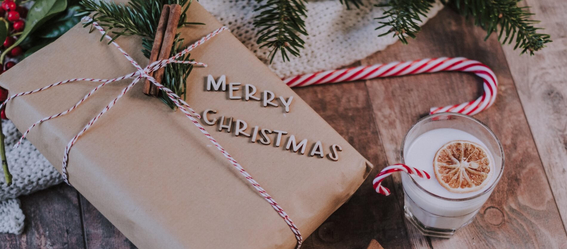 Paper wrapped Christmas present on a table with a glass of milk and candy cane