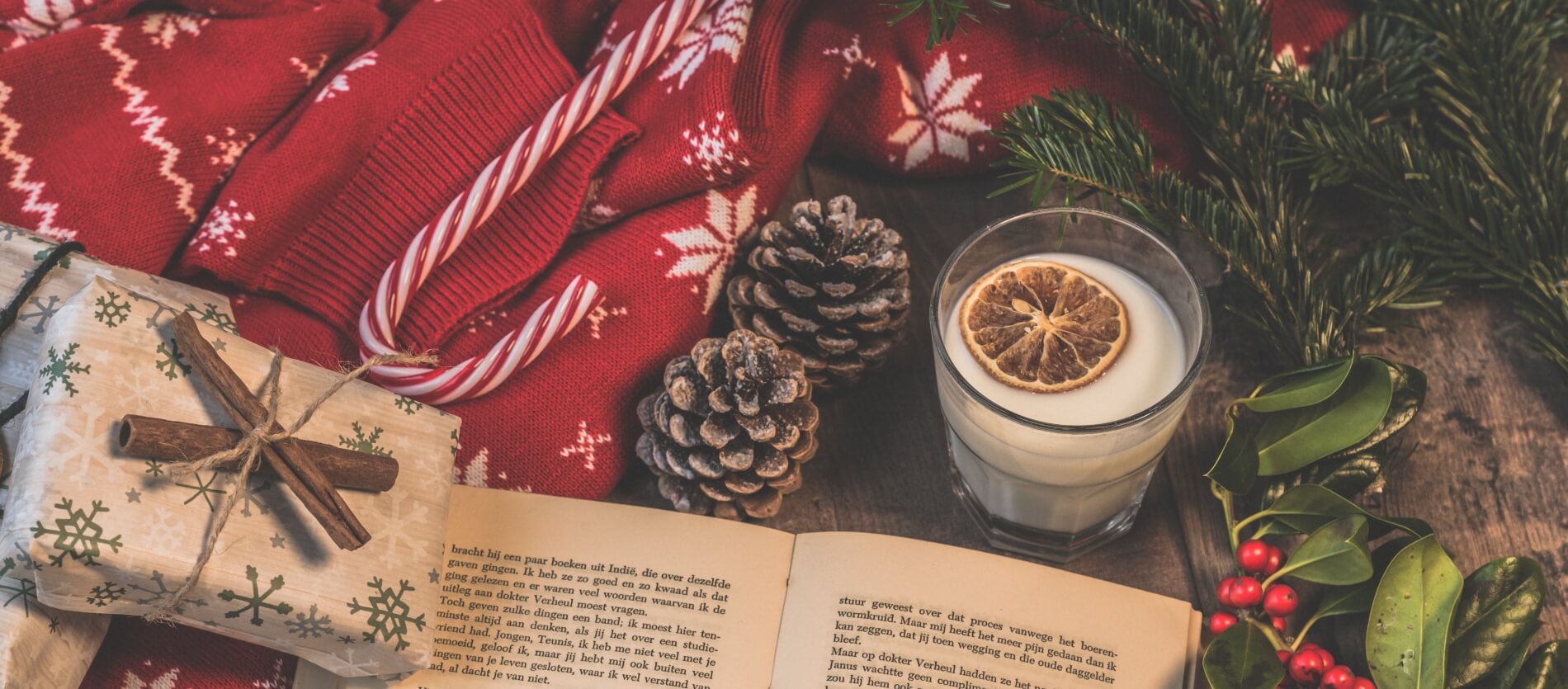 An open book with Christmas present, pine cones, candy cane and a glass of milk