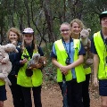 Smallgroupofsixsmilingstudentsandfouradultsholdingplushtoysofnativeanimalsinabushlandsetting