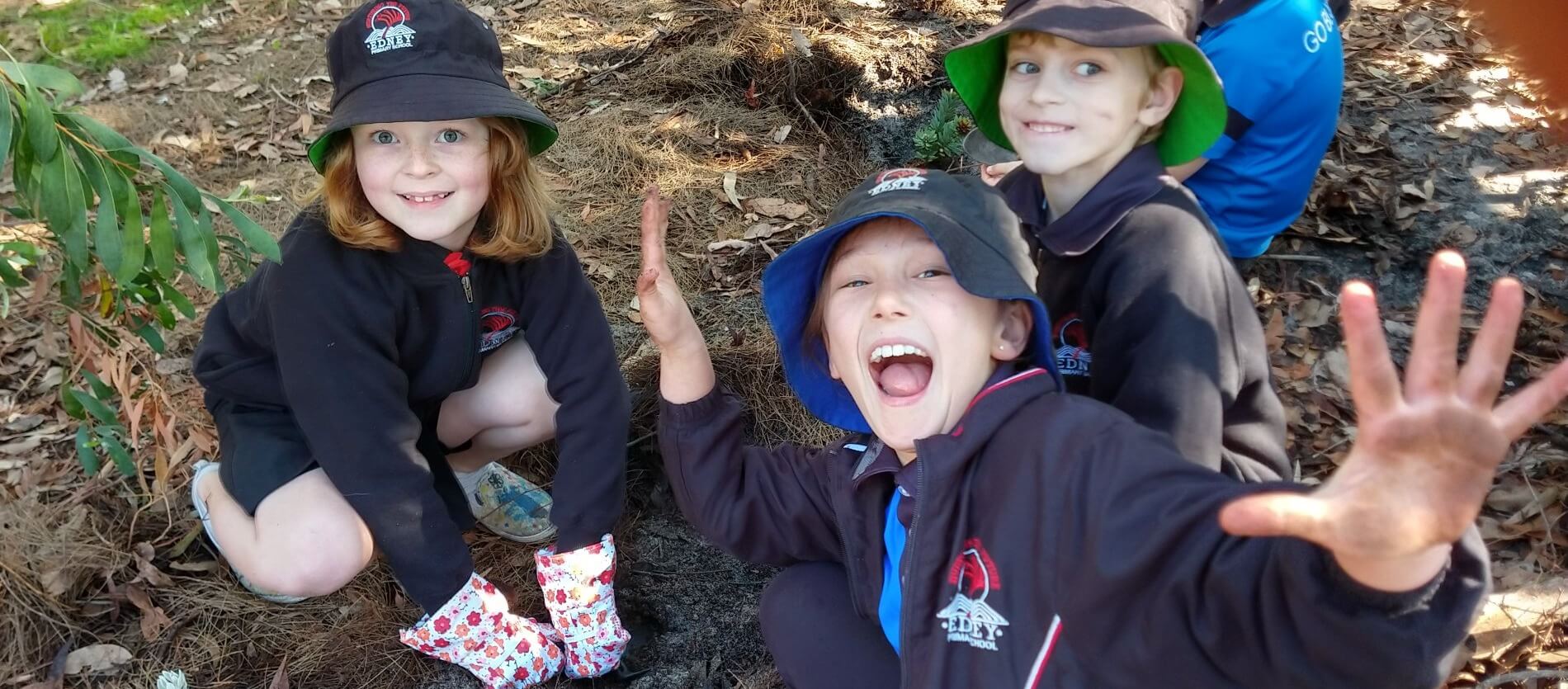 Threeprimaryschoolstudentsagirlandtwoboyssmilingandwavingtheirhandsinexcitementaboutplantingyoungseedlings