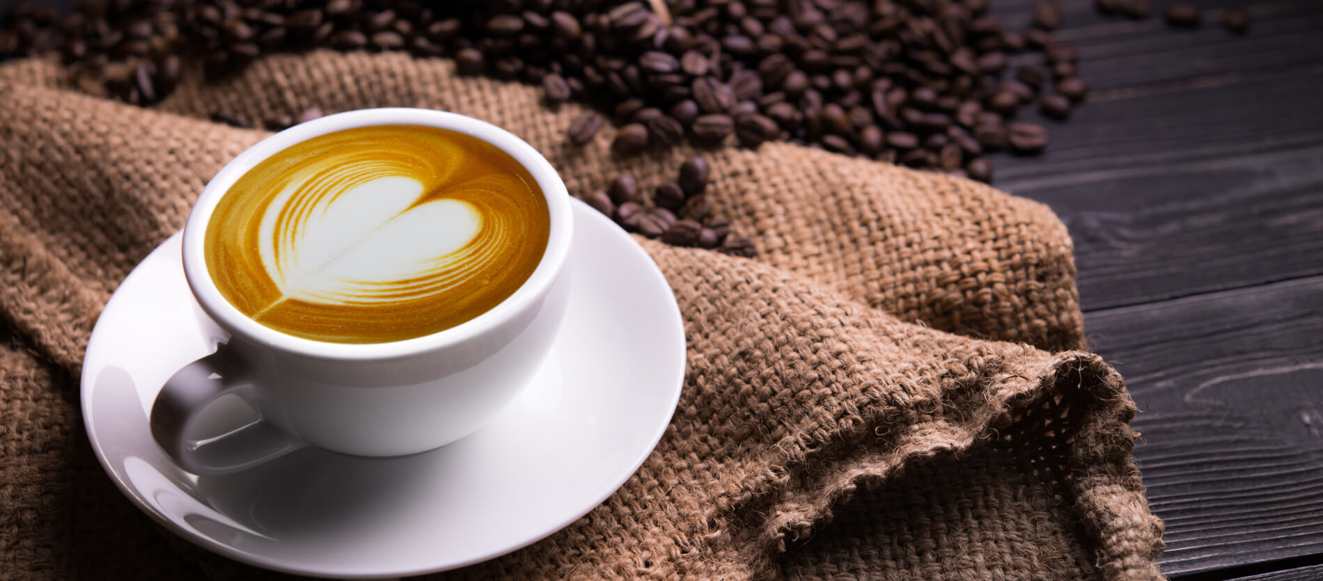 A cup of coffee on a hesin cloth with coffee beans 