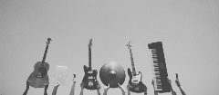 Eight various musical instruments being held up. Image is in black & white