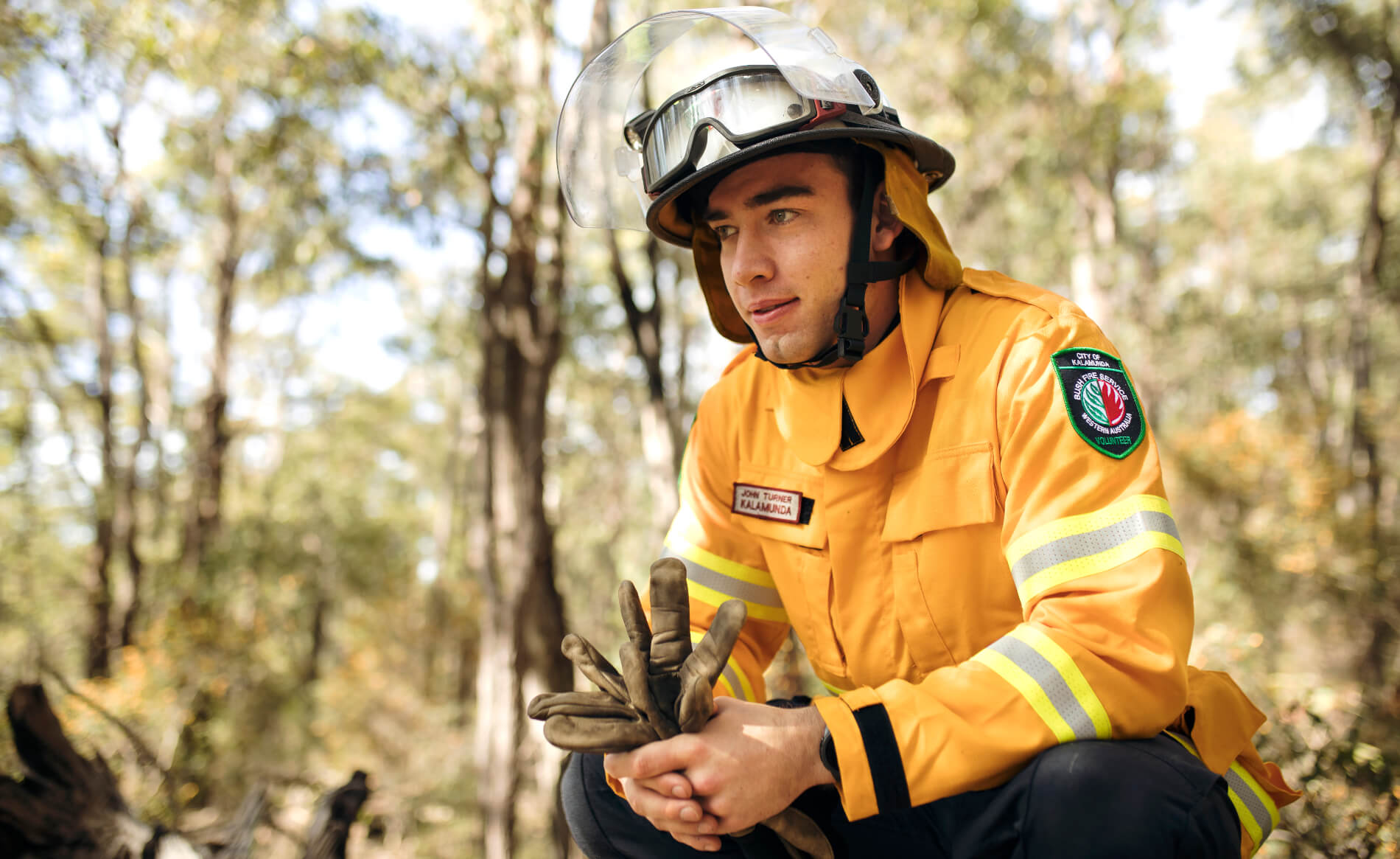 A local fire crew member in protective gear, crouching and holding a pair of gloves