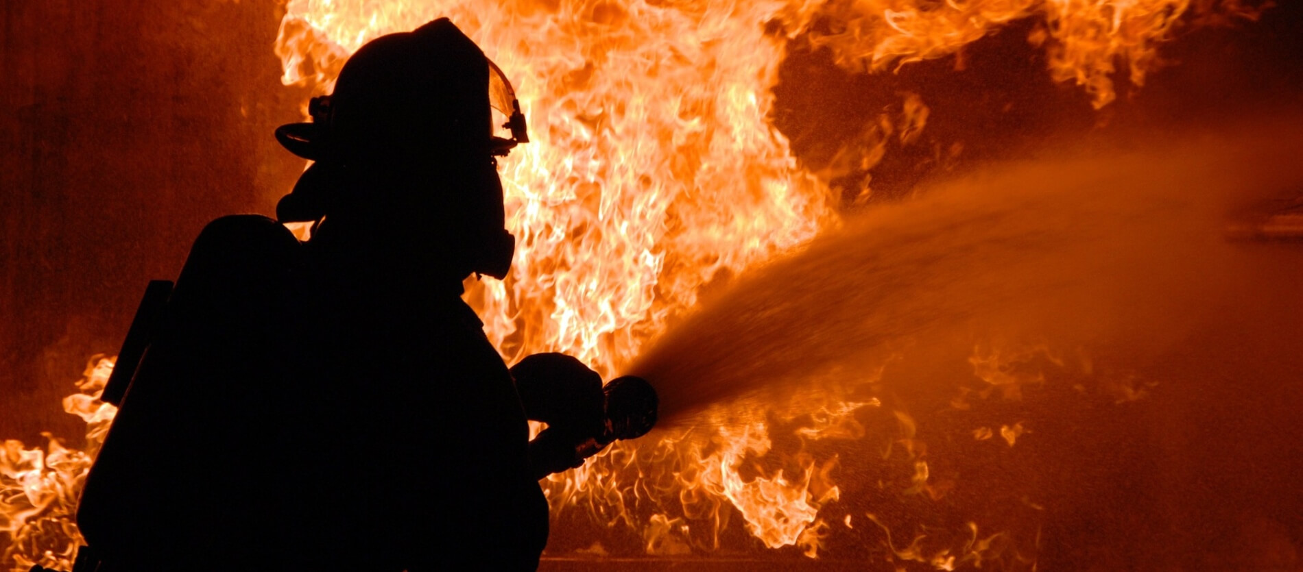 A firefighter silhouette who is hosing a large fire in front of them