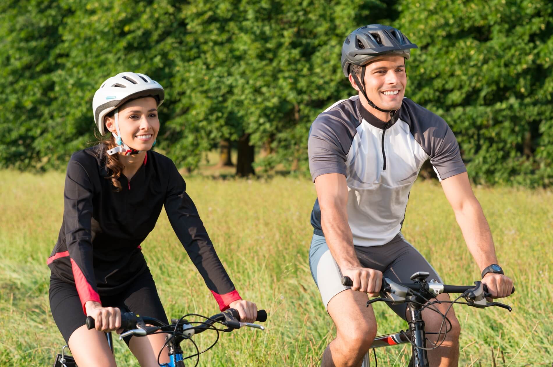 A young couple riding mountain style bicycles on a long grassy landscape