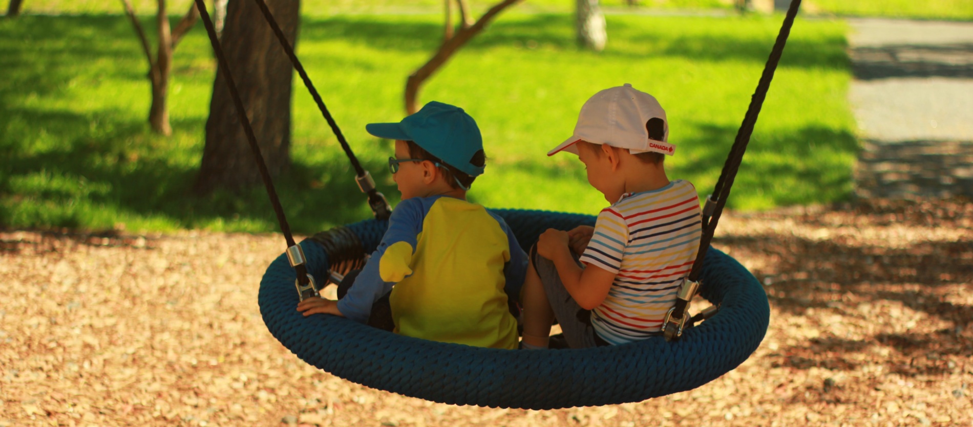 Two young kids swinging on a spider web swing